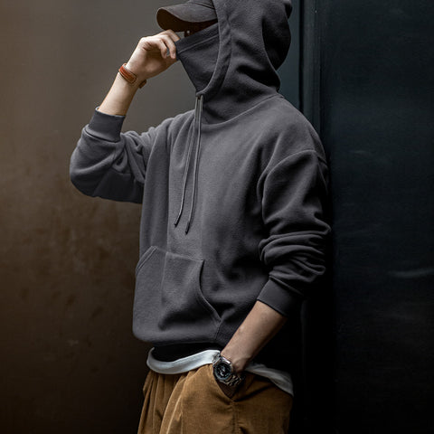 Person wearing a dark gray hoodie and brown pants against a dark background