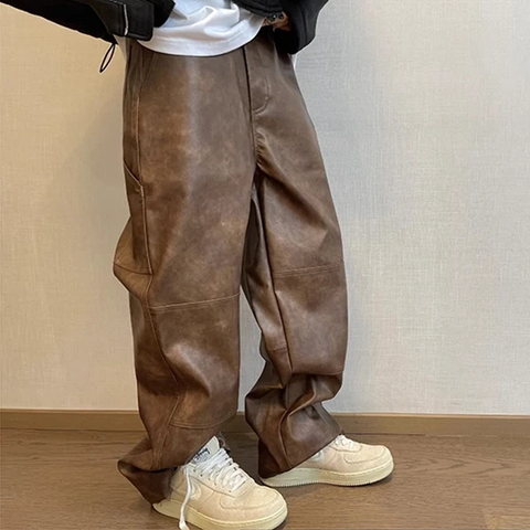 Person wearing brown leather pants and white sneakers against a neutral background