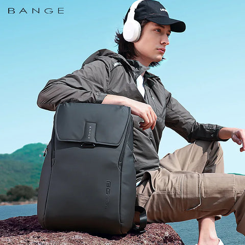 Person sitting on a rock with a Bange backpack, wearing headphones, and mountains in the background.