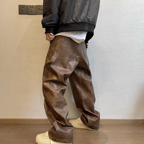 Person wearing brown leather pants and a dark jacket in a minimal indoor setting.