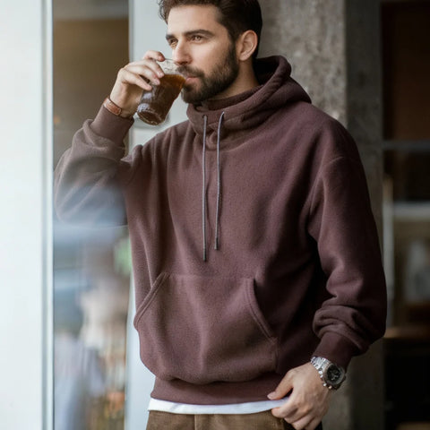 Man in a maroon hoodie drinking from a glass in a casual setting