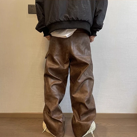 Person wearing brown leather pants against a plain wall.