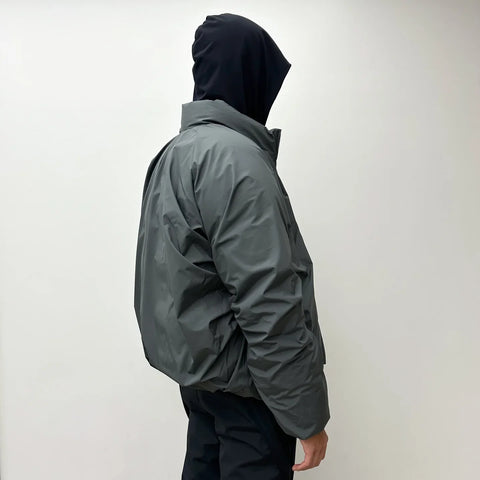 Person wearing a dark gray raincoat with a hood on a plain background